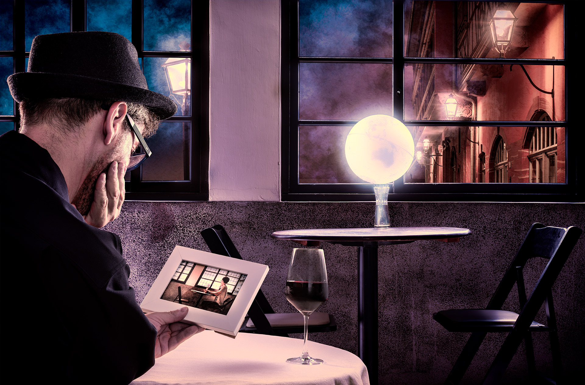 man holding photo in a dark cafe, globe glowing on another table